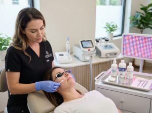 Clinician applying a glycolic acid peel in a modern medspa with microneedling, laser, RF and LED devices visible in the background