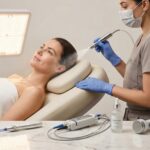 Clinician performing an oxygen facial in a modern medspa with microneedling pen, laser handpiece, chemical peel bottle, RF device and LED panel visible on the counter